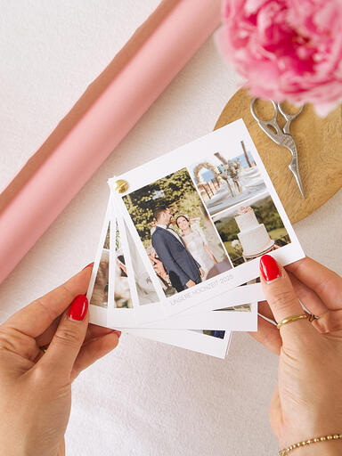 Hände halten einen quadratischen Fotofächer mit goldener Schraa