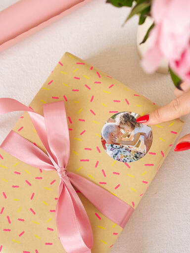 Hände kleben einen runden Fotoaufkleber auf ein liebevoll verpacktes Geschenk