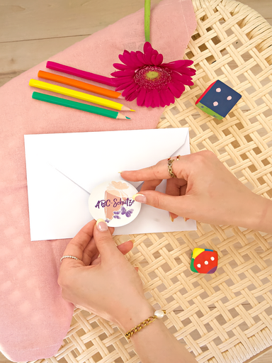 Hände kleben ein rundes Briefsiegel mit Einschulungsdesign auf die Rückseite eines weißen Umschlags