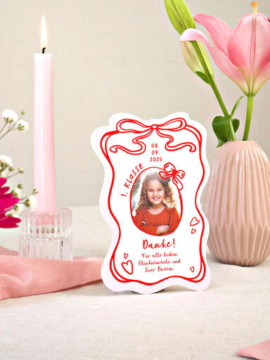 Eine Danksagungskarte zur Einschulung mit gewelltem Rand, niedlichem Schleifen-Design und Foto lehnt an einer Blumenvase