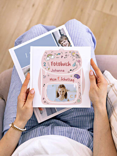 Eine Frau hält Fotobücher zur Einschulung mit Fotos und fröhlichem Design auf dem Cover in den Händen