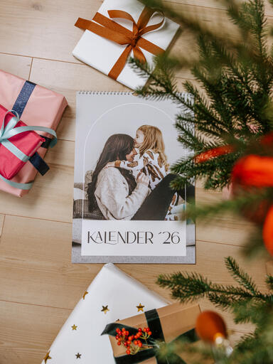 Personalisierter Foto-Wandkalender mit Spiralbindung liegt mit Geschenken unterm Weihnachtsbaum