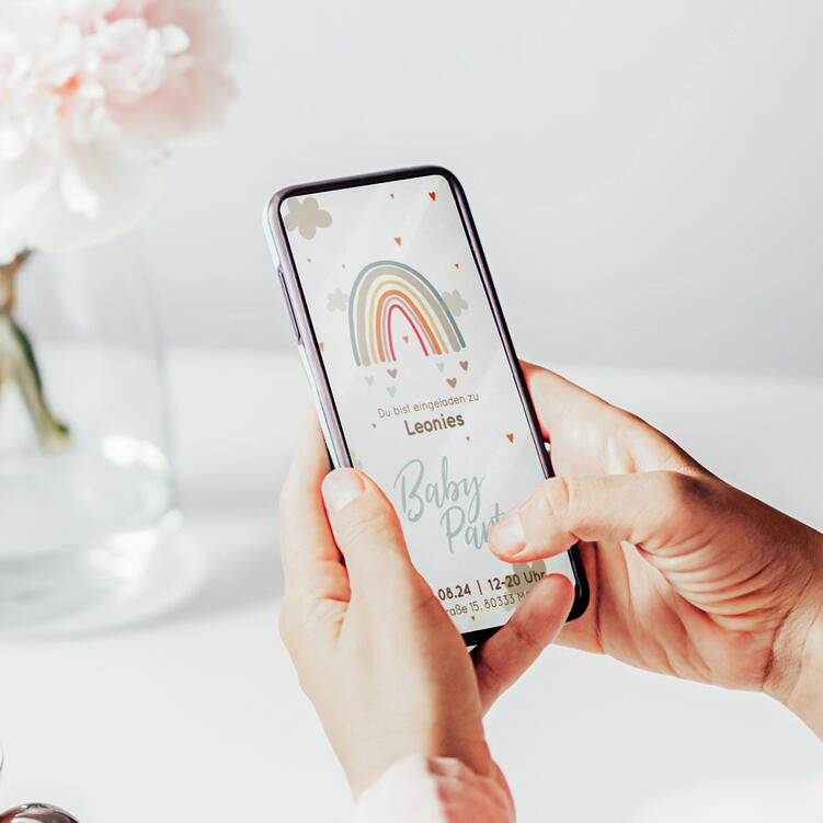 Frau schaut sich eCard zur Babyparty im 'Regenbogen-Zauber'-Design auf Smartphone an