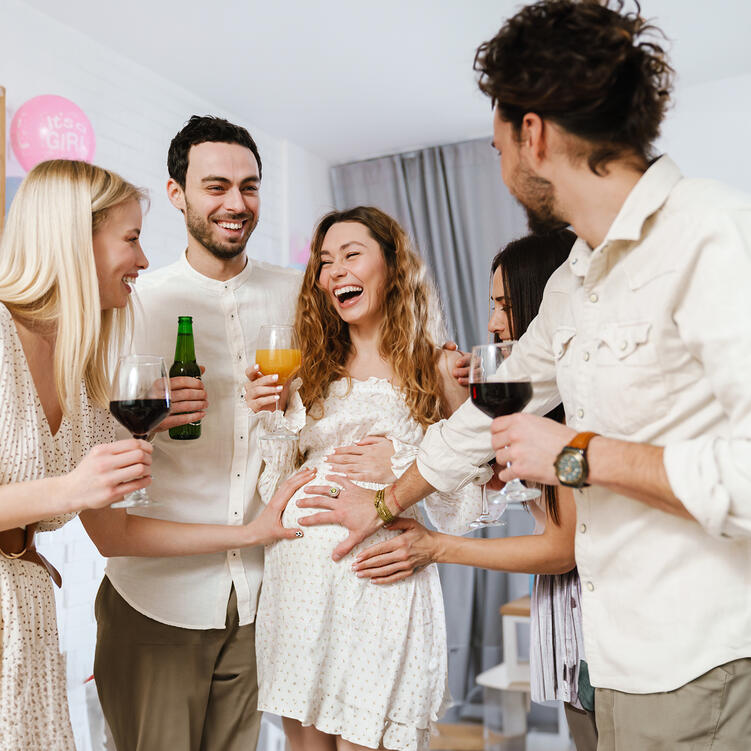 Werdende Mama mit Freunden beim Anstoßen auf Baby Shower