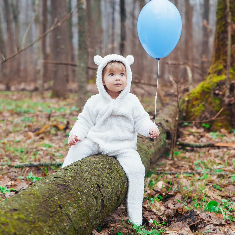 Kleines Kind im süßen Teddybär-Kostüm mit blauem Luftballon